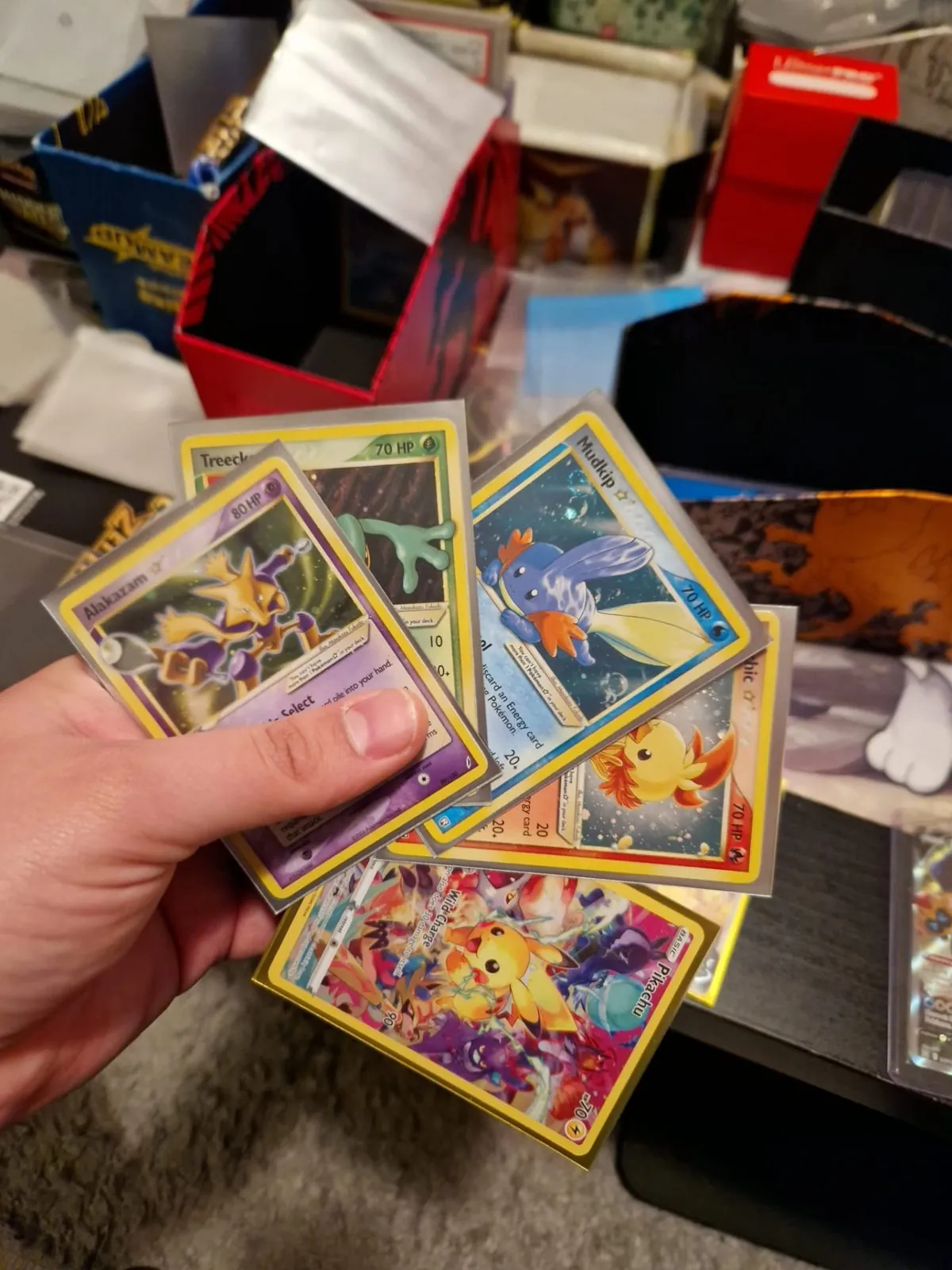 Ruka drži nekoliko Pokémon Gold Star karata: Alakazam, Mudkip, Treecko, Torchic i Pikachu